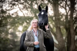 Hübsche Frau mit schwarzem Pferd unter Bäumen - emotionale Mensch-Tier-Verbindung